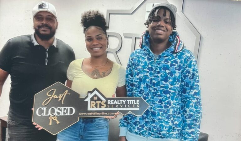 Tiffany Green, standing alongside her son, holds a real estate sign shaped as a key that reads "just closed"