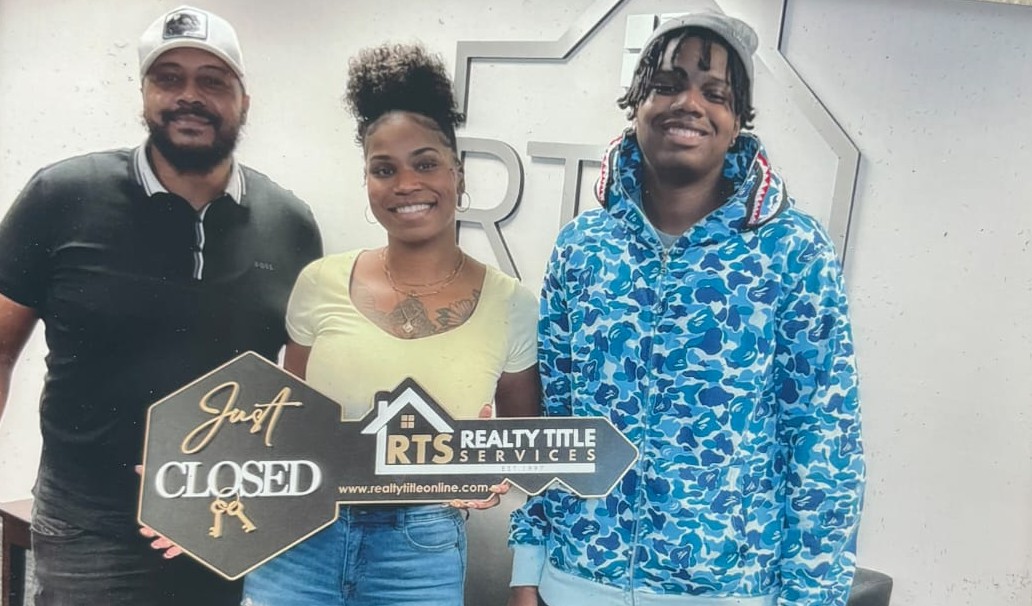 Tiffany Green, standing alongside her son, holds a real estate sign shaped as a key that reads "just closed"
